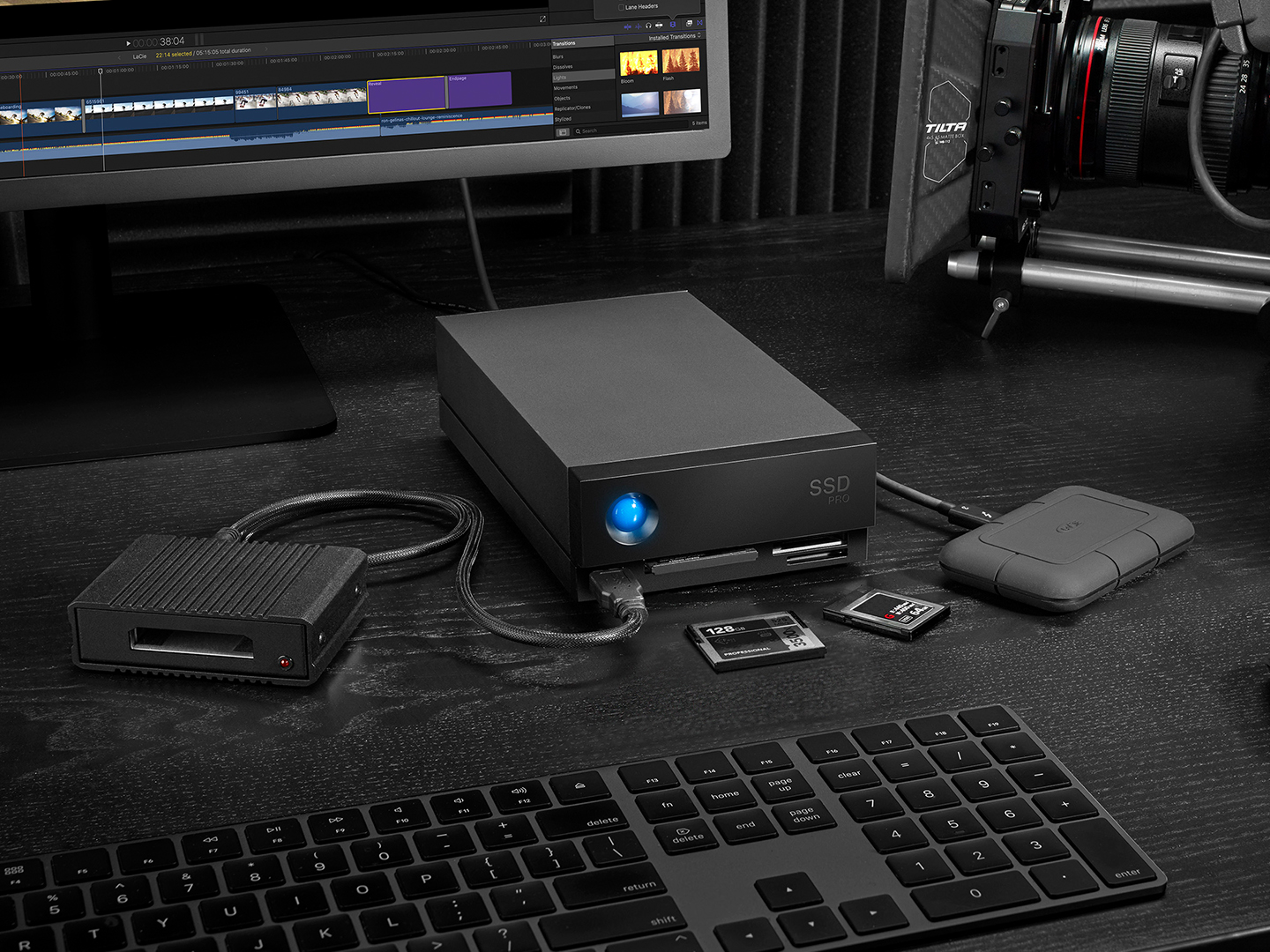 Edit studio features LaCie 2big Dock hard drive, mini drive, desktop, SSD cards, keyboard and video camera — all in black. 