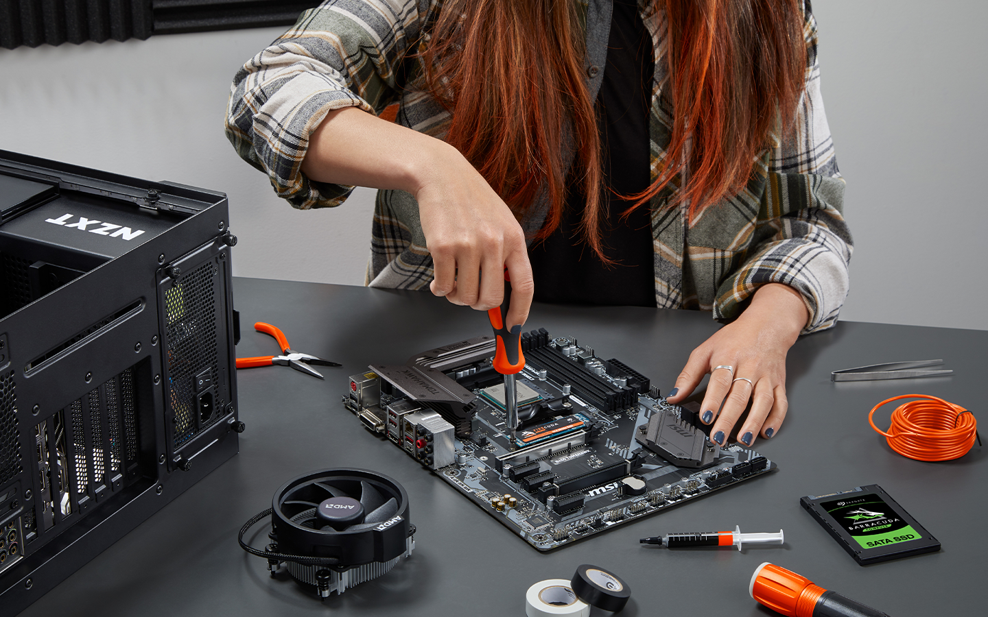 Person using a screwdriver to work on a computer motherboard with parts and tools on a desk.