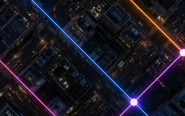 Aerial view of a city grid at night with glowing neon lines and nodes, illustrating connected AI infrastructure networks.