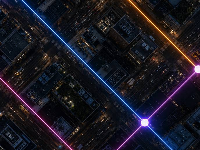 Aerial view of a city grid at night with glowing neon lines and nodes, illustrating connected AI infrastructure networks.