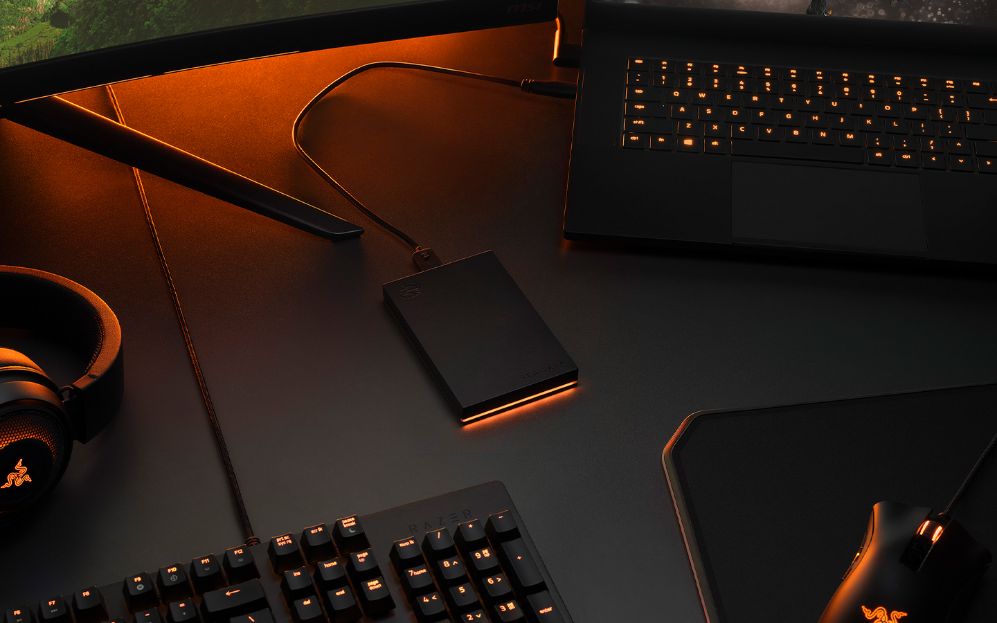 Seagate external drive enclosure sits at the center of a desk with a laptop, keyboard, headphones and mouse surrounding it.