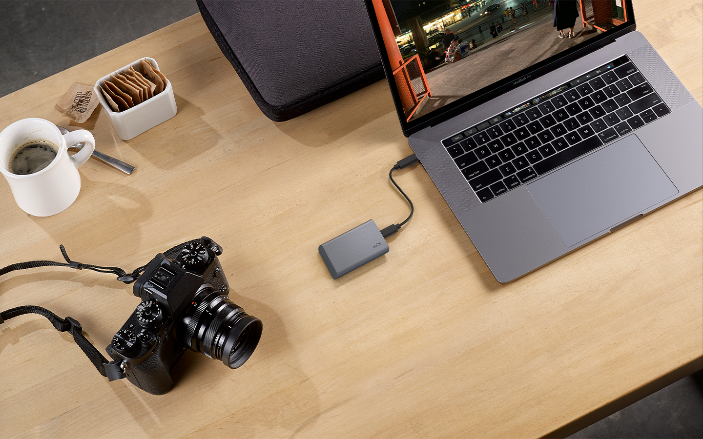 Seagate mini, portable SSD is shown connected to a laptop with a digital camera and cup of coffee nearby.