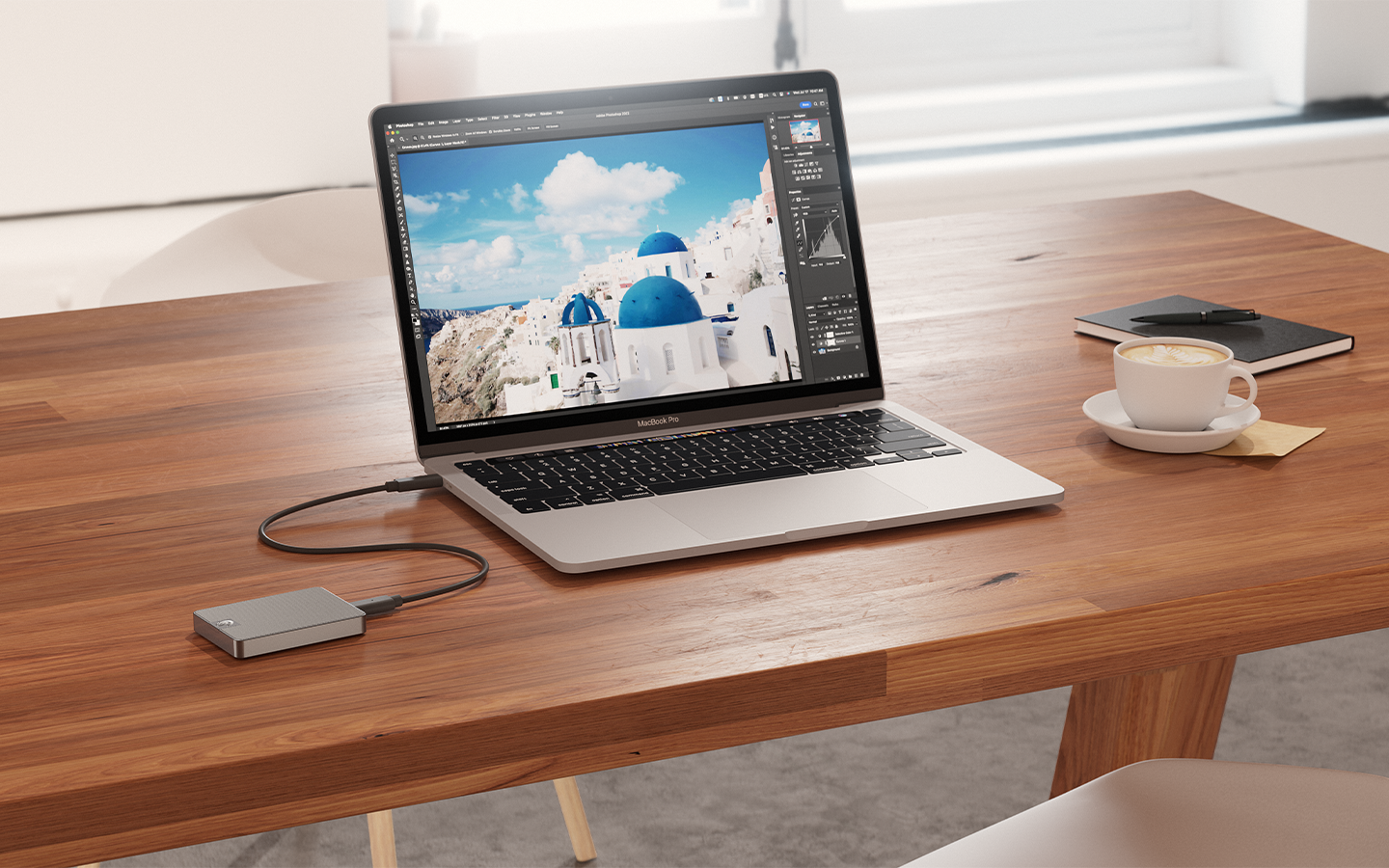 Laptop linked to Seagate portable SSD, sits beside a coffee cup, notebook, and pen—signifying ready for work or creativity on the go.