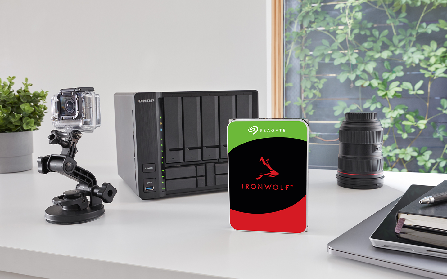 FireCuda NAS drive stands before a digital camera setup, NAS system, camera lens, and stacked laptop, tablet, and notebook.