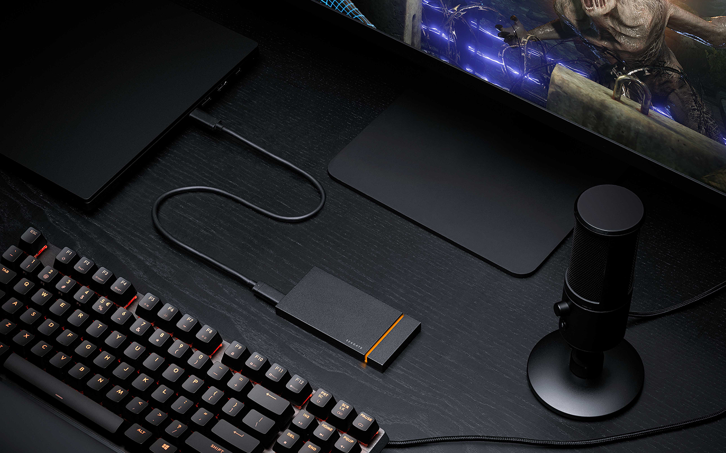 Seagate mini portable drive sits at the center of a gaming desktop screen, microphone, and keyboard.