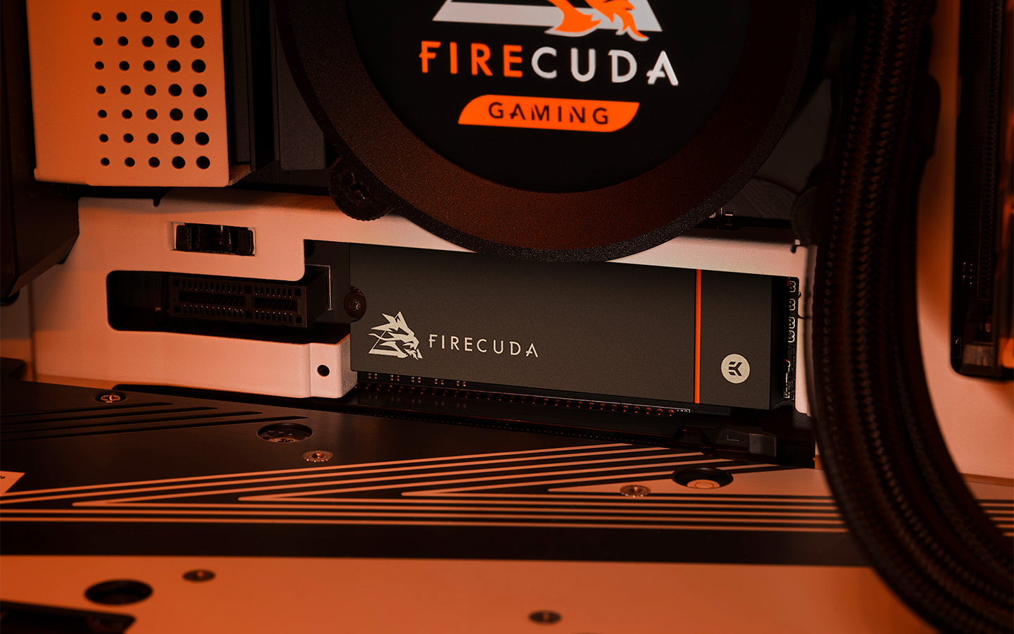 FireCuda liquid cooler mounted on a PC motherboard sits above a FireCuda NVMe SSD installed in the M.2 slot.