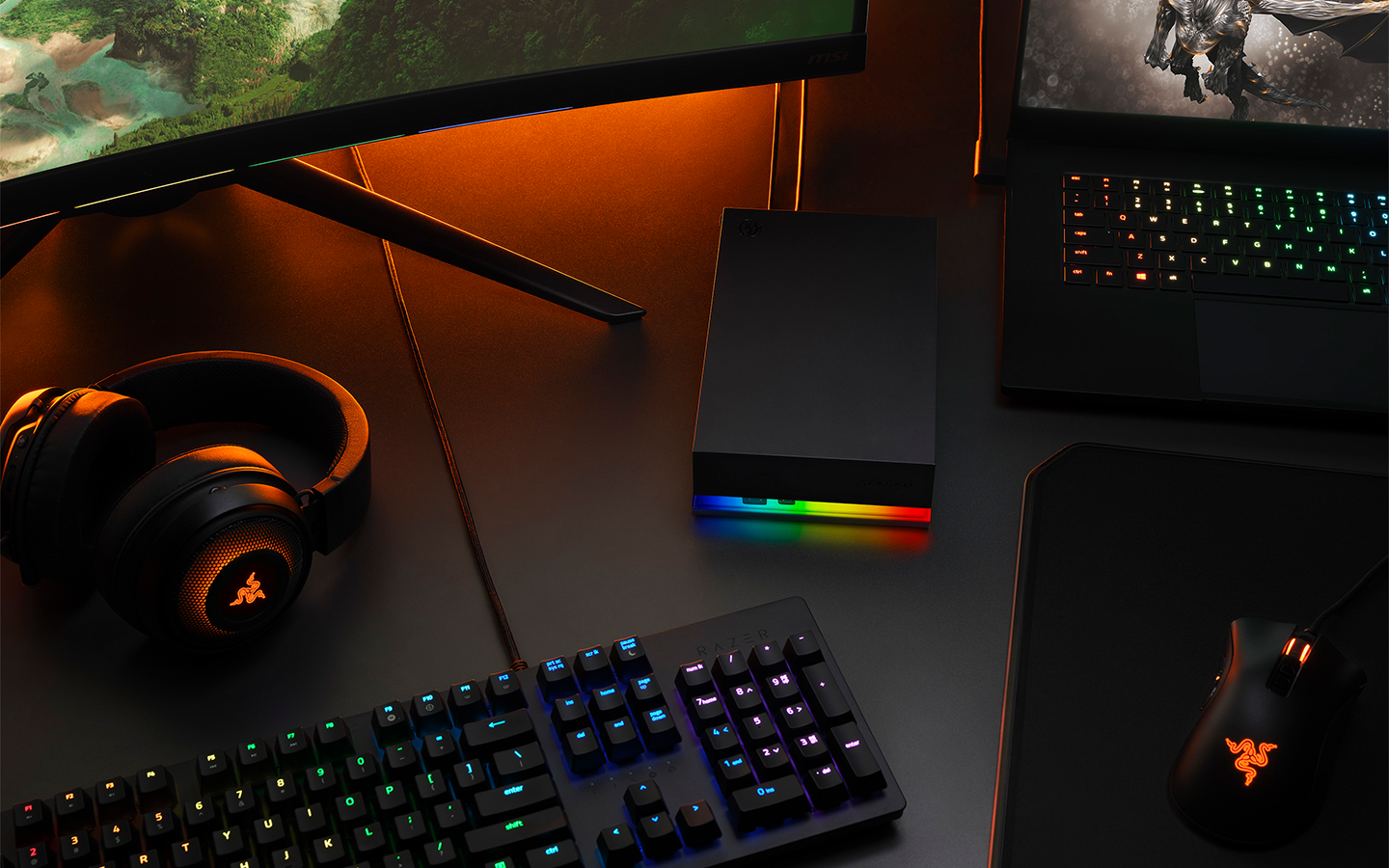 Headphones, keyboard, computer gaming screen, and laptop surround a Seagate FireCuda external gaming SSD.
