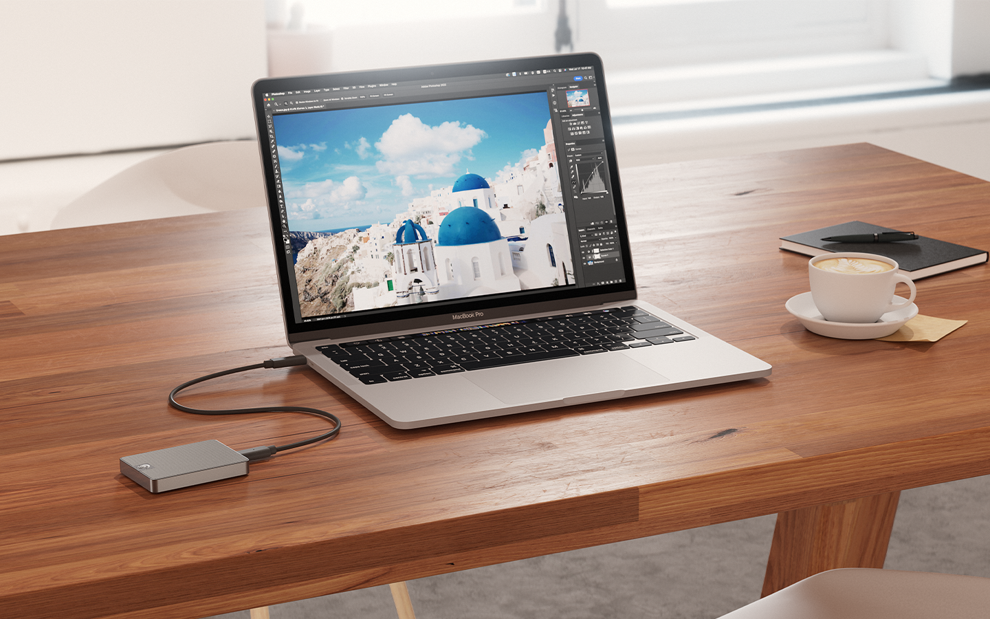 Laptop linked to Seagate portable SSD, sits beside a coffee cup, notebook, and pen—signifying ready for work or creativity on the go.
