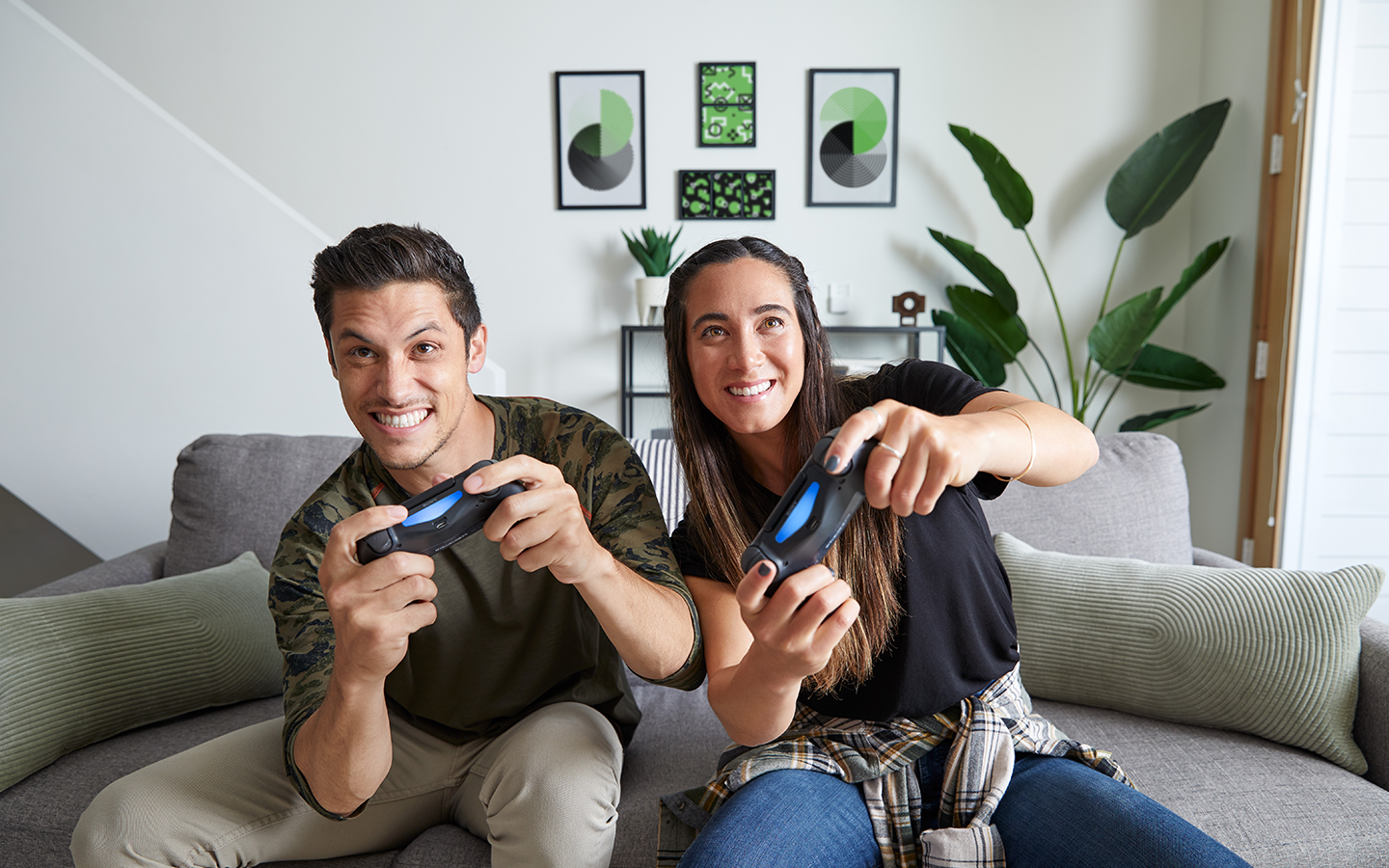 Two people sit on a couch holding game controllers to play a videogame.