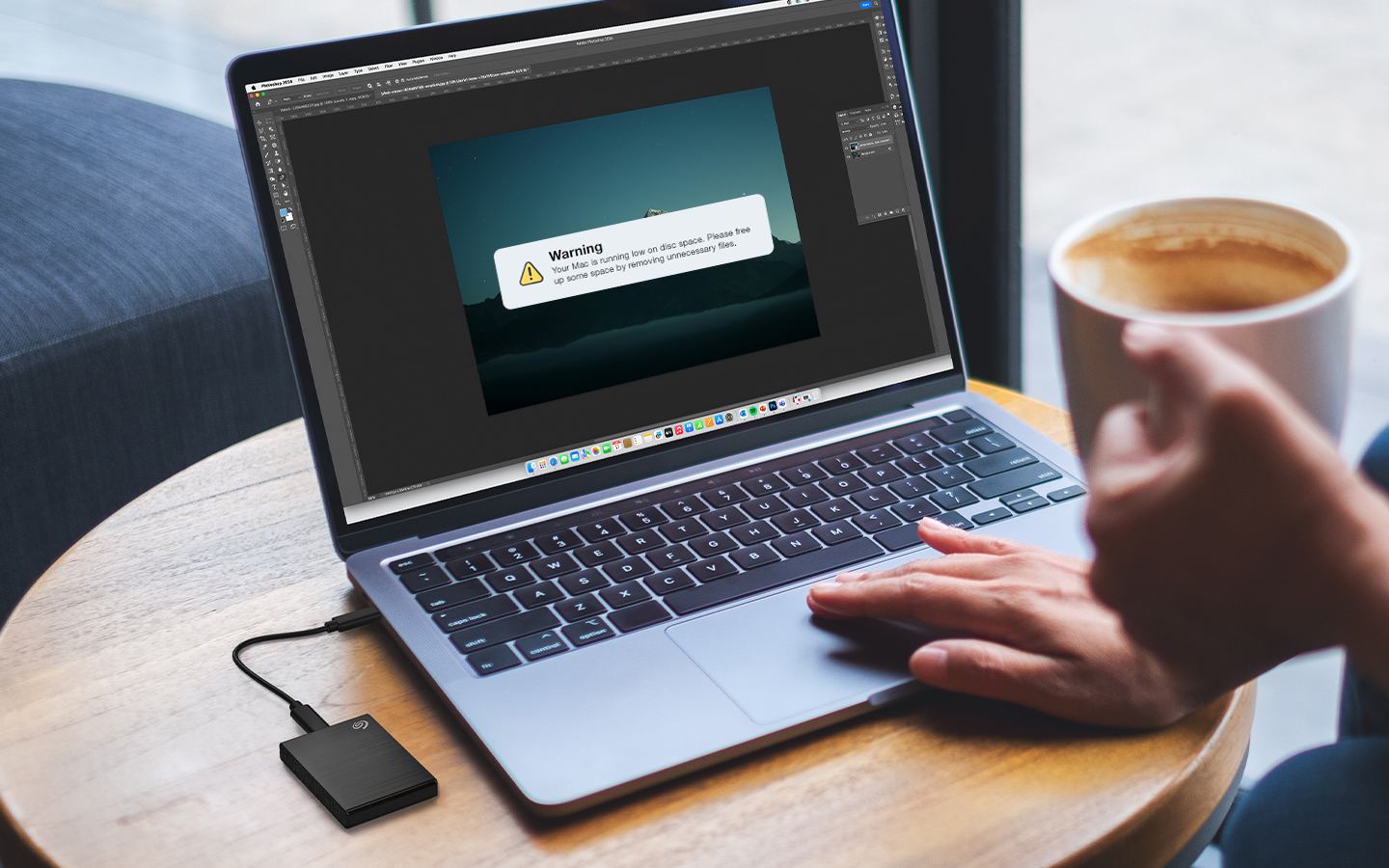 Person holding a cup of coffee uses the track pad of a laptop that’s connected to a Seagate external drive.
