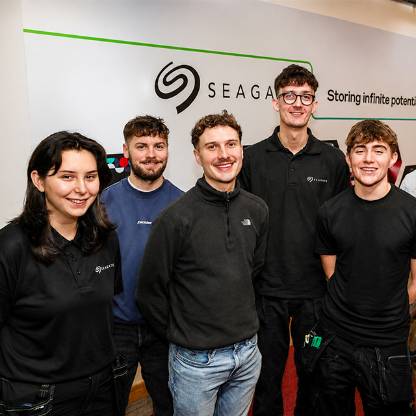 Five people smile for a photo in front of a Seagate banner displaying the message, “Storing infinite possibilities."