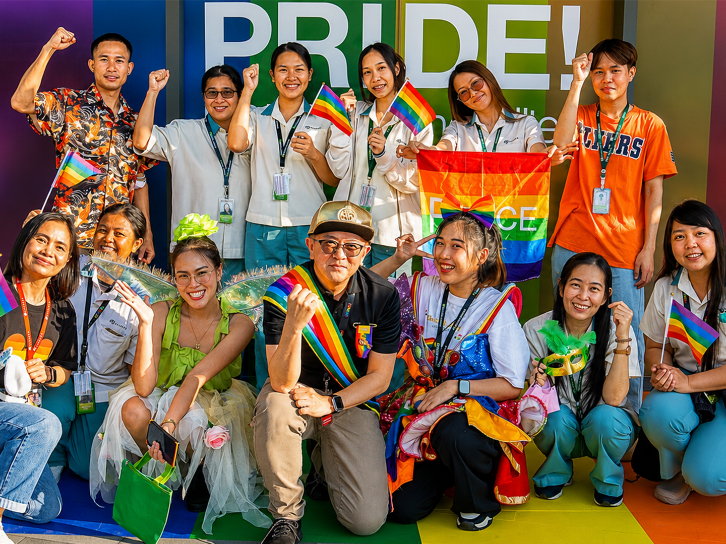 Group gathers with rainbow flags for a photo in front of a Pride banner.