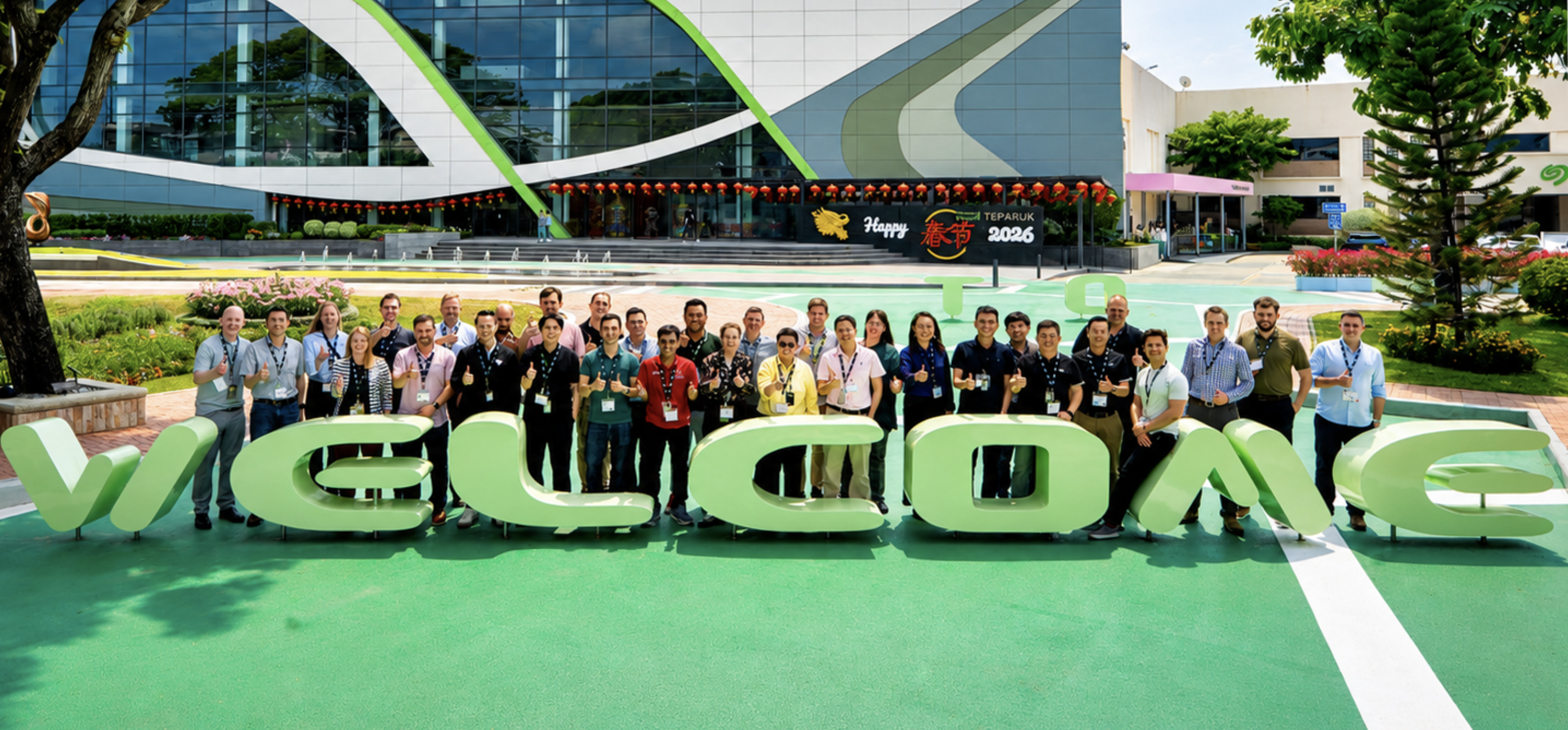 Group of people pose outdoors behind large 3D letters that spell the word welcome.