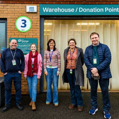 Five people stand outside a building entrance beneath a sign reading “Warehouse/Donation Point.” 