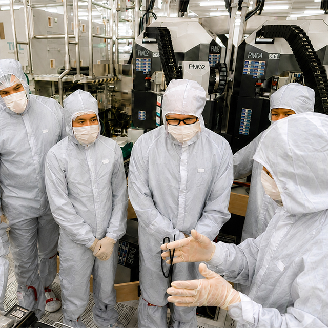 Team members in clean room suits gather around equipment on a manufacturing floor. 