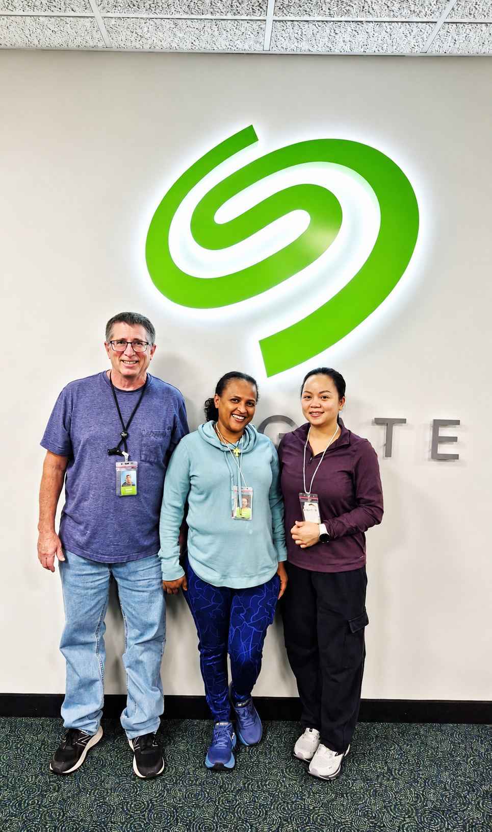 Three people pose for a photo with an illuminated Seagate swirl logo displayed on the wall behind them.