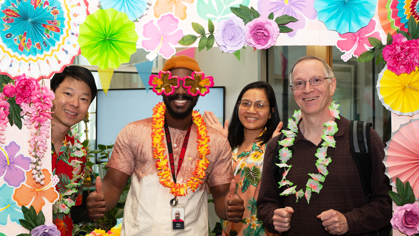 Print out from a photo booth featuring a luau-themed frame shows four people wearing leis, Hawaiian shirts and fun sunglasses.