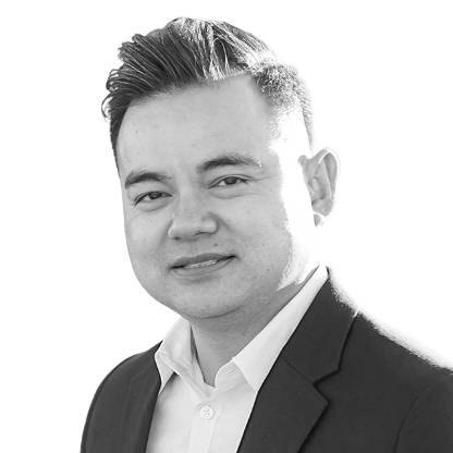 Seagate Senior Product Marketing Manager Hac Tran is shown wearing a white collared shirt and dark blazer in an outdoor headshot with a softly blurred background.