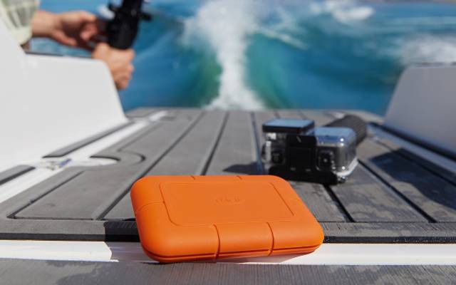 LaCie Rugged SSD sits on a boat next to a waterproof camera and a person filming, highlighting durability and portability.