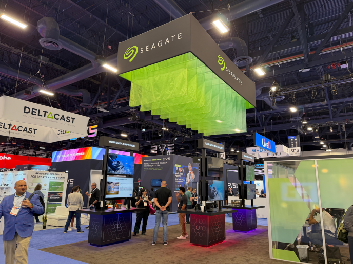 Seagate trade show booth with suspended green fabric panels, branded cube signage, demo kiosks, and attendees at NAB 2026.