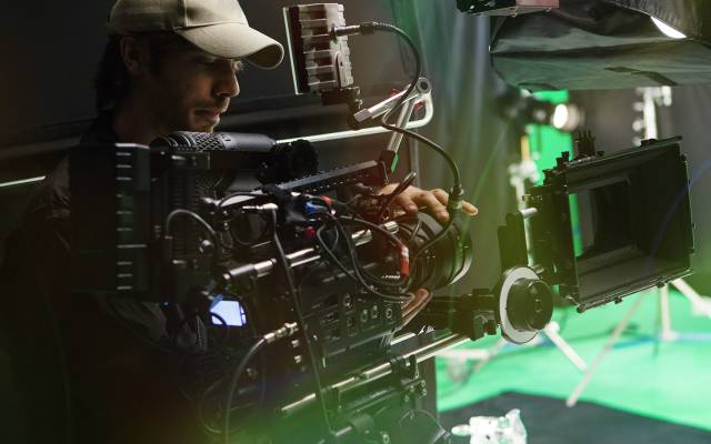 Camera operator adjusts a large professional rig in a green screen studio, illustrating the surge in high-quality video production.