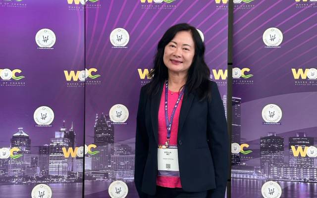 Stella Wu, senior engineering director of media research and development, stands before a conference backdrop wearing a blue suit and pink top.
