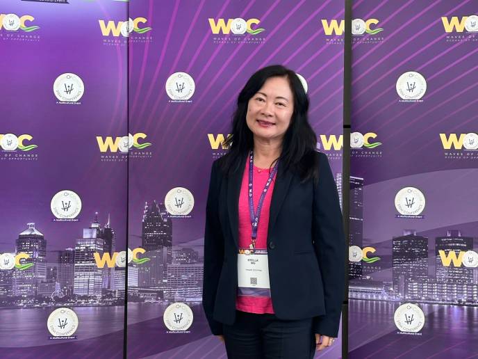 Stella Wu, senior engineering director of media research and development, stands before a conference backdrop wearing a blue suit and pink top.