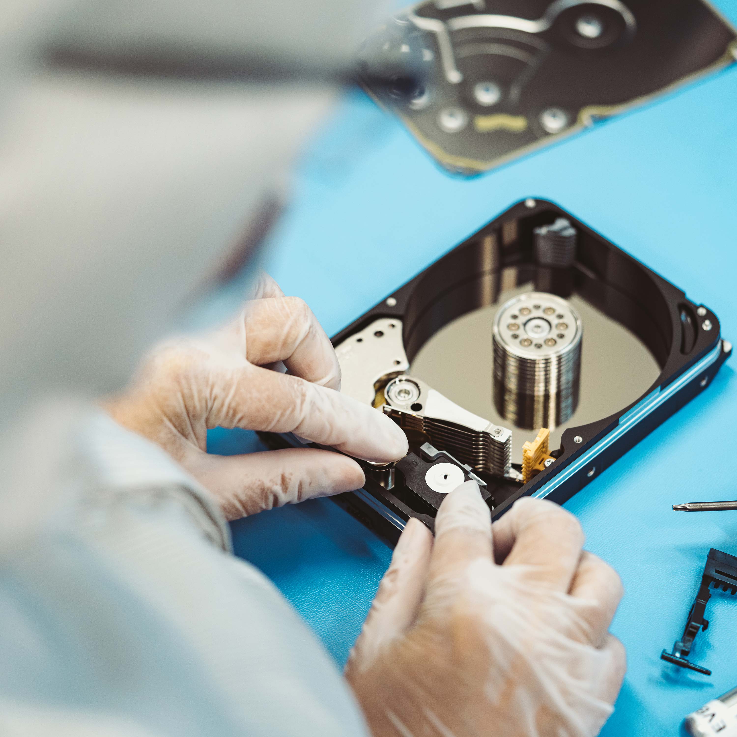 A gloved worker assembles a drive with a screwdriver shown to the side.