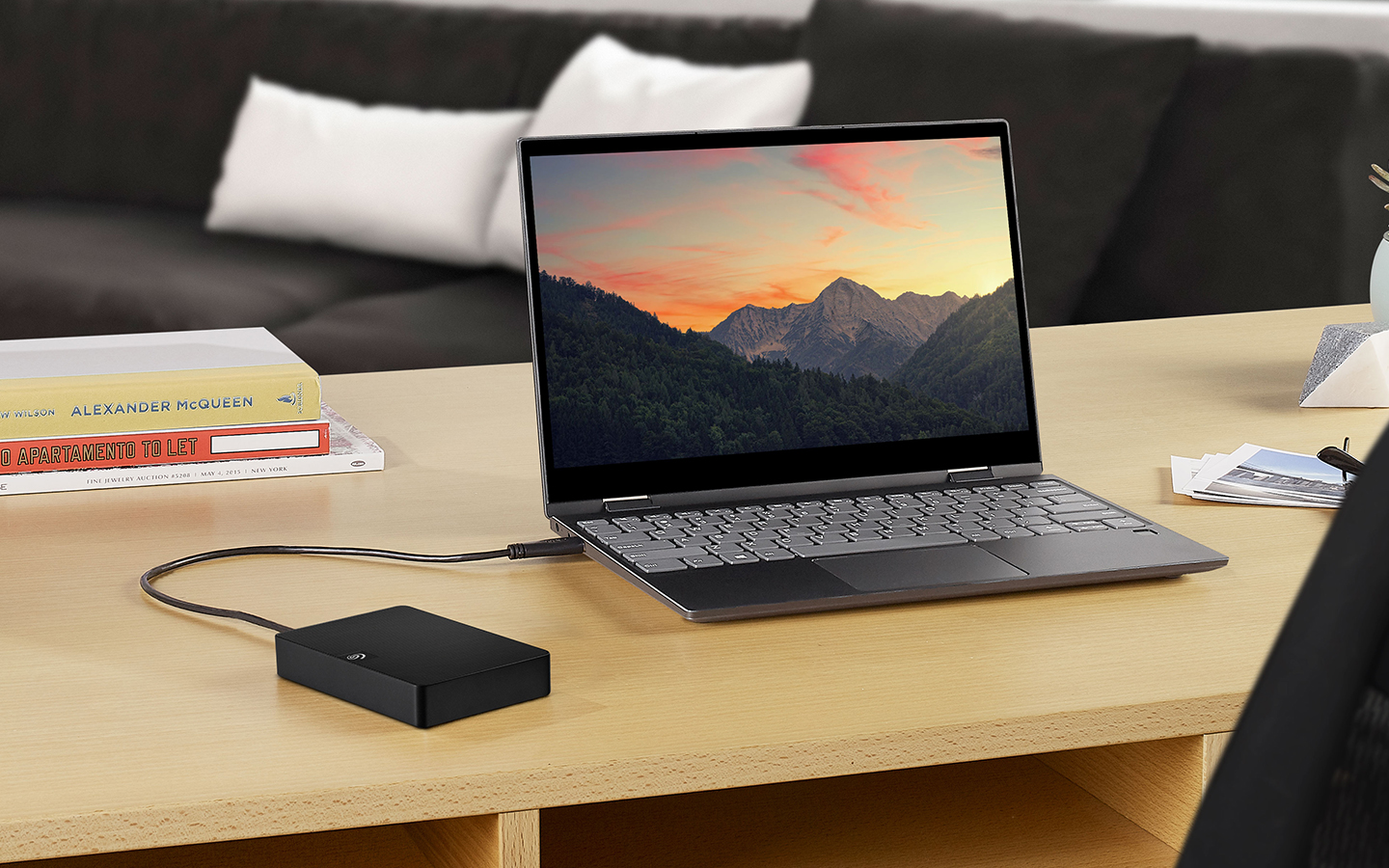 Laptop on a desk in a home office setting is plugged into a silver portable Seagate One Touch external drive.